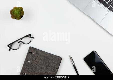 Modern unisex working space, top view. Notepad, pen, cactus, smartphone, glasses on white background, copy space, flat lay. Desktop of freelancer. Wor Stock Photo