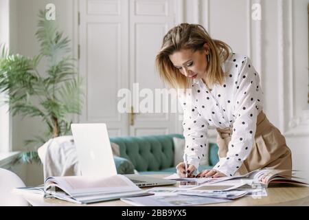 Fashion designer stylist working on new project in the studio, using laptop, magazines, sketches..woman freelancer Stock Photo