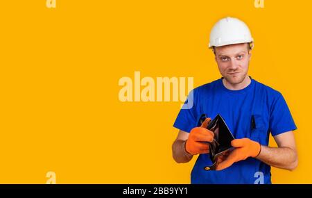 The puzzled worker in overalls holds his empty purse without money. The concept of economic crisis, unemployment and production, coronavirus, pandemic, health. Stock Photo