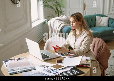 Fashion designer stylist working on new project in the studio, using laptop, magazines, sketches..woman freelancer Stock Photo
