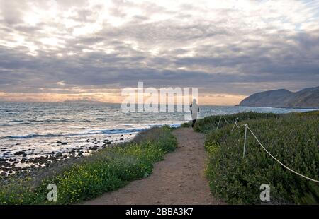 Woman walking on trail on cliffs above the Pacific Ocean at Malibu on the Southern California coast. Stock Photo