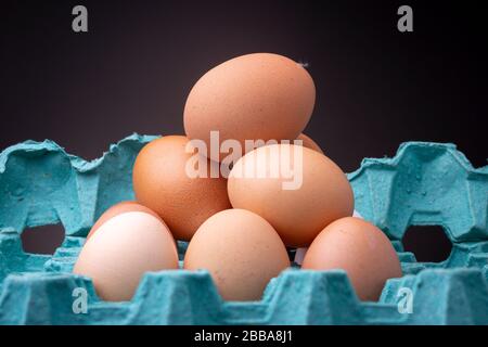 Teal colourful egg carton box with well lit stack of brown shaded chicken eggs contrasted against a dark studio background Stock Photo