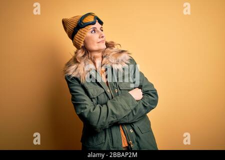 Middle age beautiful blonde skier woman wearing snow sportwear and ski goggles looking to the side with arms crossed convinced and confident Stock Photo