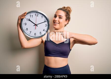 Young beautiful blonde sportswoman wearing sportswear on time to do sport holding clock very happy pointing with hand and finger Stock Photo