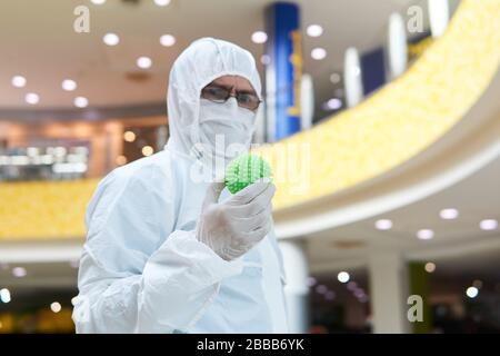man in coverall disposable anti-epidemic antibacterial isolation suit suspiciously holds in his hand a rubber ball resembling a macro photo of a virus Stock Photo