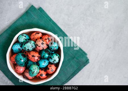 Painted red and blue quail eggs for Easter in small ceramic plate on green napkin on gray concrete background. Empty place for text and sign. Stock Photo