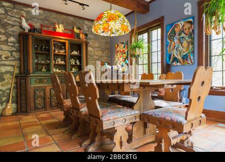 Wooden handcrafted dining table with Navaho patterned upholstered high back chairs, hand-carved buffet in dining room with terracotta ceramic tile flooring and fieldstone wall inside an old circa 1830 Quebecois style country home, Quebec, Canada. This image is property released. CUPR0357