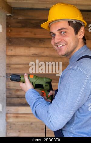 Portrait of a handsome young craftsman with yellow hard hat holding an electric drill Stock Photo