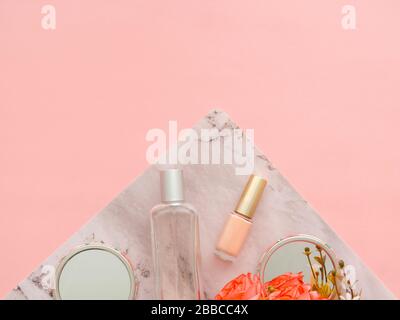 Roses flowers, perfume, mirrors and nail polish bottle on two colors pink and marble colors with copy space as background. Flat lay composition, magaz Stock Photo