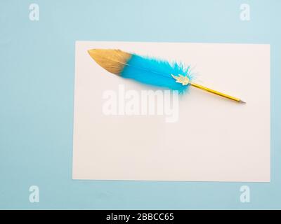 Blue and golden feather quill pen resting on white blank parchment blank paper with copy space for your text message isolated on light blue pastel bac Stock Photo