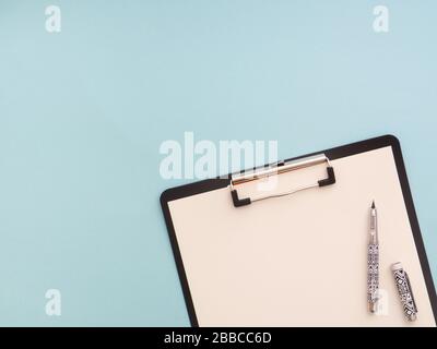 Clipboard with white sheet and pen isolated on a blue color background. View from above, flat lay, copy space for text. Minimalistic design, workspace Stock Photo