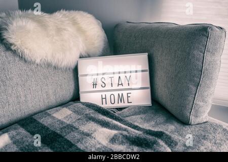 Coronavirus home lightbox sign with hashtag message Hashtag STAYHOME glowing on home sofa with cozy lambswool fur, blanket. COVID-19 text to promote self isolation staying at home. Stock Photo