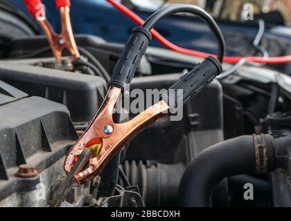 Jump cables on car low power battery. Black and red. Broken car start attempt. Selective focus. Stock Photo