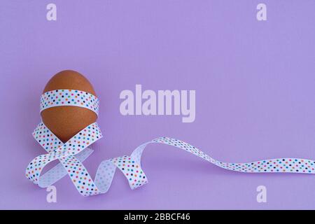 Egg standing on cup, on a soft purple background. Easter egg tied with a festive ribbon Stock Photo