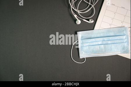Top view of office table at home during coronavirus outbreak with kear phones, calendar and surgical face mask. Copy space. Work remotely or work from Stock Photo
