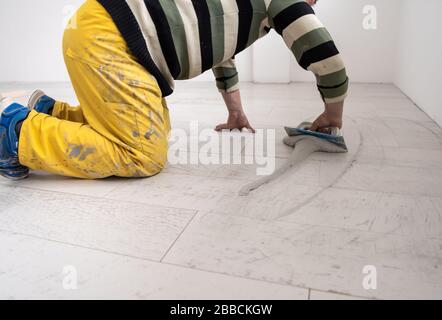 Grouting ceramic tiles. Tilers filling the space between ceramic wood effect tiles using a rubber trowel on the floor in new modern apartment Stock Photo
