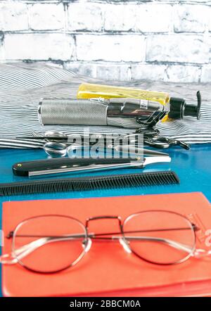 Hairdressing tools set, Red notepad with glasses and scissors, hair clipper, comb, dangerous razor, hair gel stand on blue background Stock Photo
