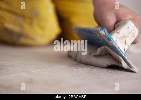 Grouting ceramic tiles. Tilers filling the space between ceramic wood effect tiles using a rubber trowel on the floor in new modern apartment Stock Photo