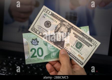 A hand holding two banknotes, one of twenty American dollars and the other of twenty Canadian dollars Stock Photo