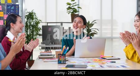 Asian female leader and ux/ui designer clapping hand for successful of mobile app interface wireframe design on table at modern office.Creative digita Stock Photo
