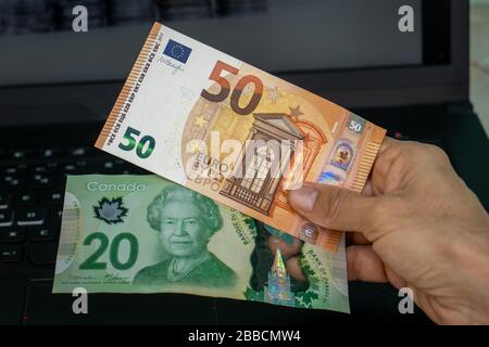 A hand holding two banknotes, one of twenty canadian dollars and the other of fifty euros Stock Photo