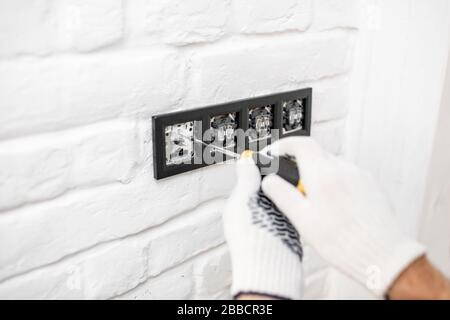 Electrician installing sockets and switches on the white brick wall, close-up Stock Photo