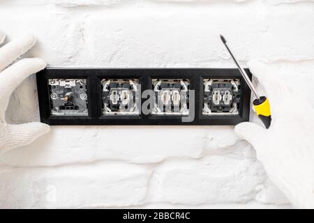 Electrician installing sockets and switches on the white brick wall, close-up Stock Photo