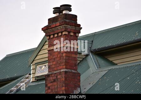 Vintage brick chimney on old house with corrugated iron roof. Stock Photo