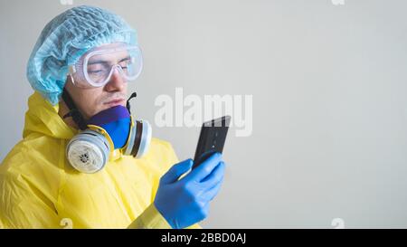 Medical worker in protective gear using smartphone after a shift. Concept of covid-19 epidemic, healthcare personell and overworking in hospitals. Stock Photo