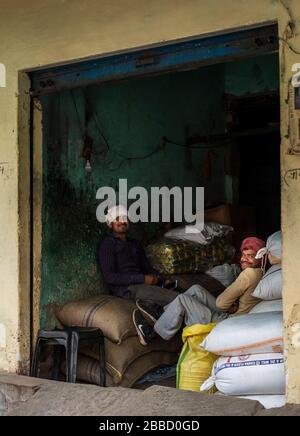 two Indian men sitting on bags in a basic wholesale store Stock Photo