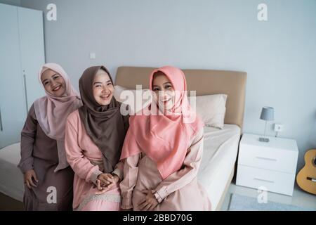 smiling three hijab women sitting on the bed in the bedroom when looking at the camera Stock Photo