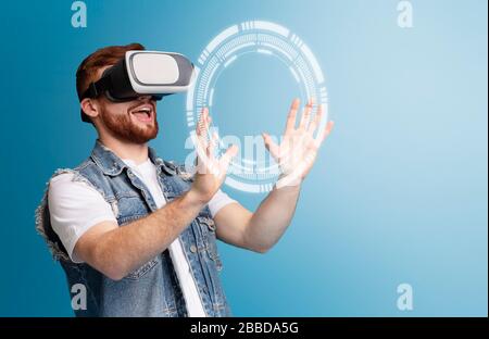 Happy young guy touching virtual screen in VR headset on blue background, empty space. Collage Stock Photo