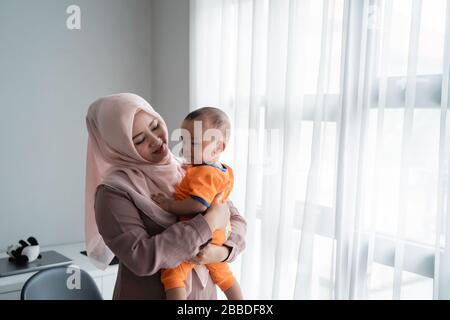 Asian moslem mother carrying her little boy when playing near window at the morning after wake up Stock Photo