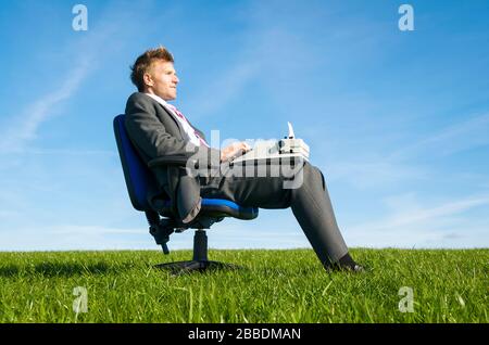 Profile portrait of man in suit sitting outdoors in office chair looking pensive while typing on old-fashioned typewriter Stock Photo