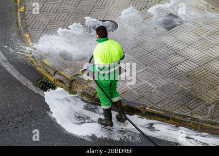 Worker holding a hose cleaning the sidewalk with water and detergent. Maintenance or cleaning concept Stock Photo