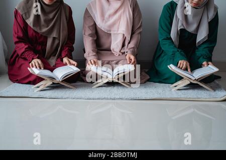 three young women wearing hijabs read the holy book of the Al-Quran together in the room Stock Photo