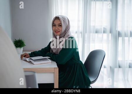 asian hijab women smiling when sit on the chair study and reading the holy book of Al-quran in the bedroom Stock Photo