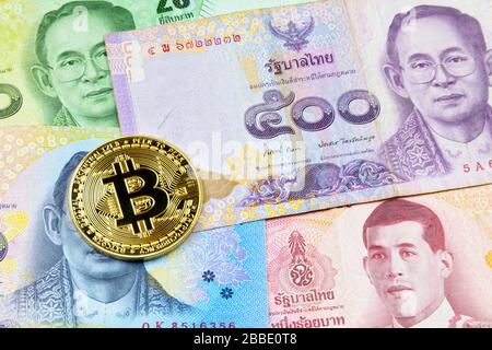 Close-up on a golden Bitcoin coin on top of a stack of Thai Baht banknotes. Stock Photo