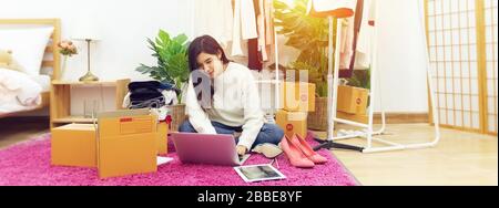 work from home. happy female selling products online, start up small business owner using laptop computer on wooden floor with fashion clothes accesso Stock Photo
