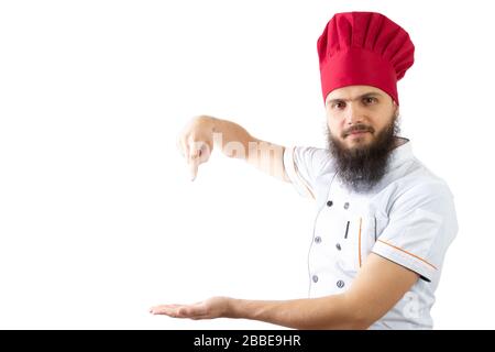 The cook points with forefinger to an empty place on palm. Bearded male chef in a red cap and white shirt isolated on a white background. Smile on the Stock Photo