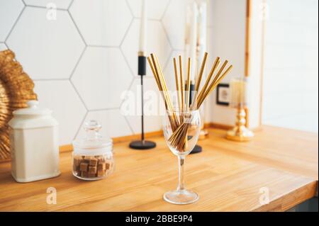 Gold paper tubes for drinks in a glass glass in a cozy wooden bright kitchen. Stock Photo