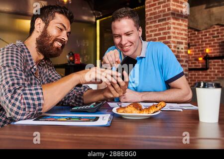 Cheerful project managers discussing interface of new mobile application on smartpphone they created when meeting at cafe Stock Photo