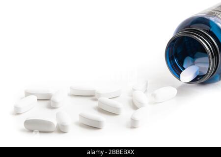 Medication bottle and white pills spilled on white background Stock Photo