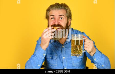 Consume alcohol. Enjoy your meal. Beer and food. Dinner at pub. Hungry man drink beer and eat snacks. Bar restaurant. Cheerful man bearded hipster drinking beer. Friday party concept. Good appetite. Stock Photo