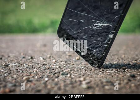 Closeup of a modern black smartphone falling on hard asphalt, hit by the corner of the screen and broken. The display is cracking. Stock Photo