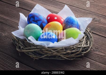 Colored painted easter eggs in a nest of twigs with white napkins on a wooden rustic background. Stock Photo