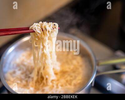 Close up of instant noodles on chopsticks while cooking over a kitchen stove with copy space Stock Photo