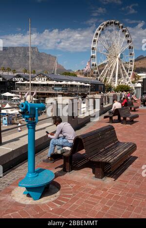 South Africa, Western Cape, Cape Town, Victoria and Alfred Waterfront, visitors sat in sunshine at waterside seating Stock Photo