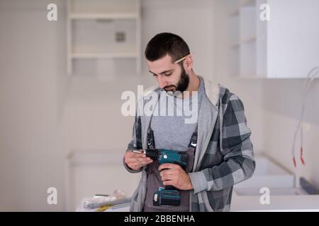 young professional worker preparing a hand drilling machine while installing a new stylish modern kitchen furniture Stock Photo