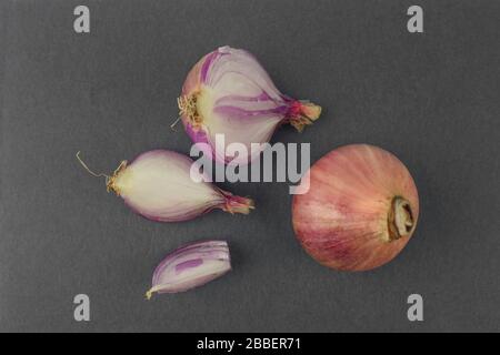 Some pieces of peeled pink colored onion scattered beside an unpeeled red onion before a dark background Stock Photo